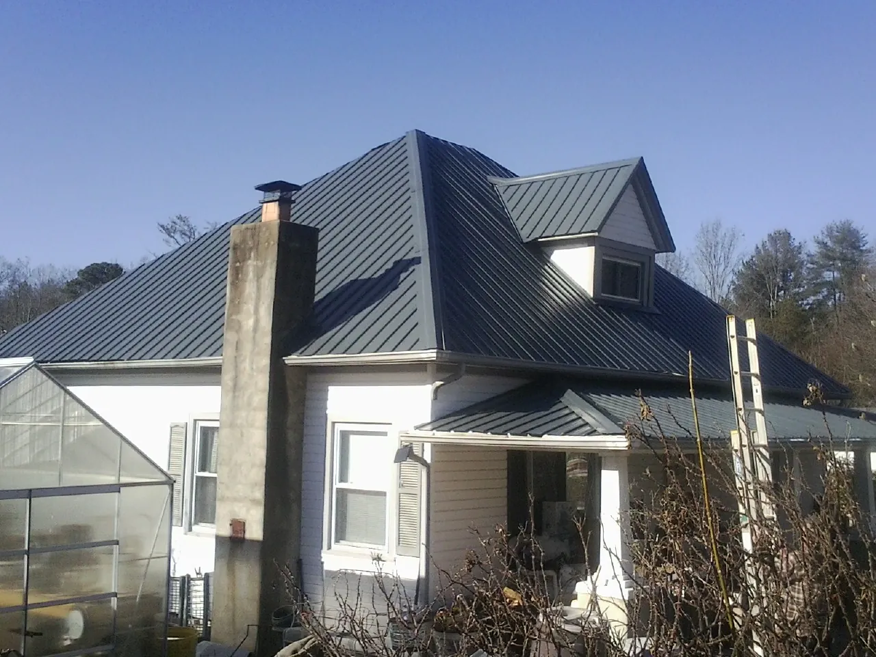 Dark blue standing seam metal roof on a white farmhouse with dormer — Slate & Tile Roof Repair by Roofing Brothers in Hallstead