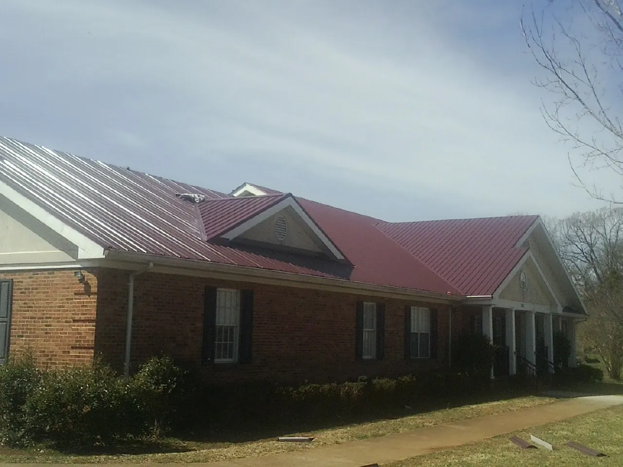 Red metal roof with gabled entries on a long brick building, from a Hail Damage Roof Repair job in Hallstead