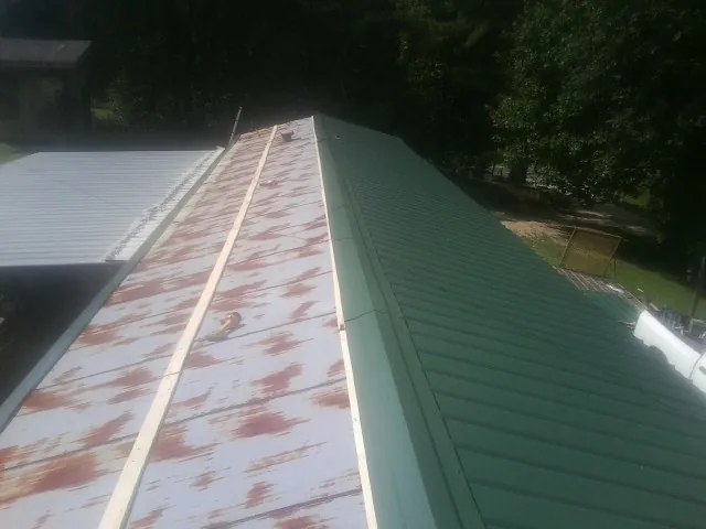 Old rusted panels beside newly installed green metal roofing — Wind Damage Roof Repair by Roofing Brothers in Hallstead
