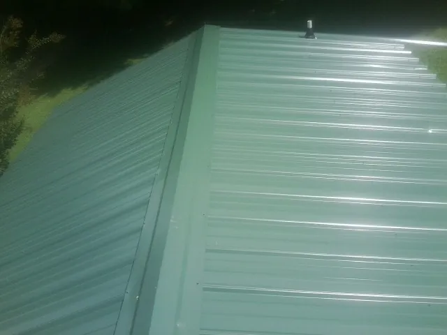 New green metal panels meeting at the ridge of a roof — Flat Roof Repair work by our crew in Hallstead