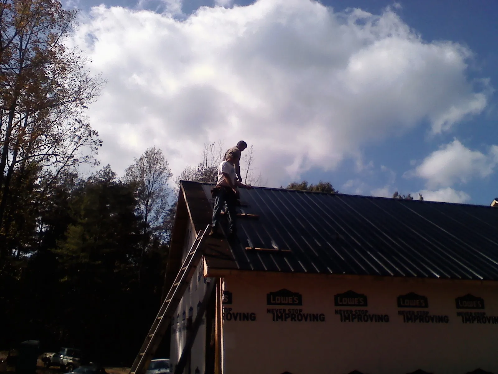Roofer fastening dark metal panels high against a cloudy sky, from a Roof Inspection job in Hallstead