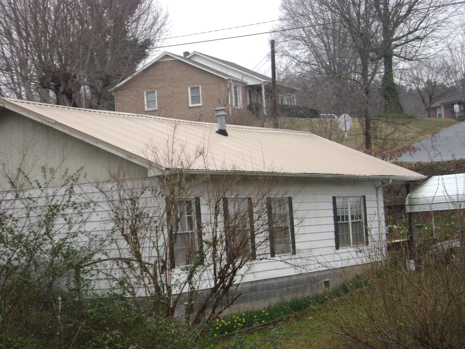 Tan metal roof on a white sided house set into a hillside — Commercial Roofing by Roofing Brothers in Hallstead