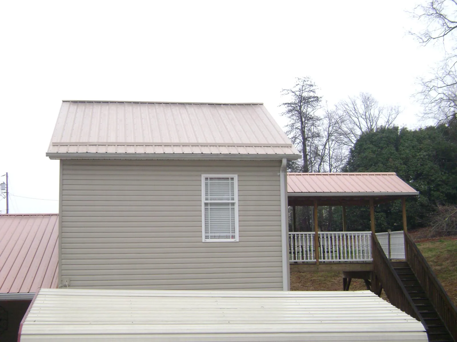 Tan metal roofs on a two story addition and attached porch, from a Roof Replacement job in Hallstead